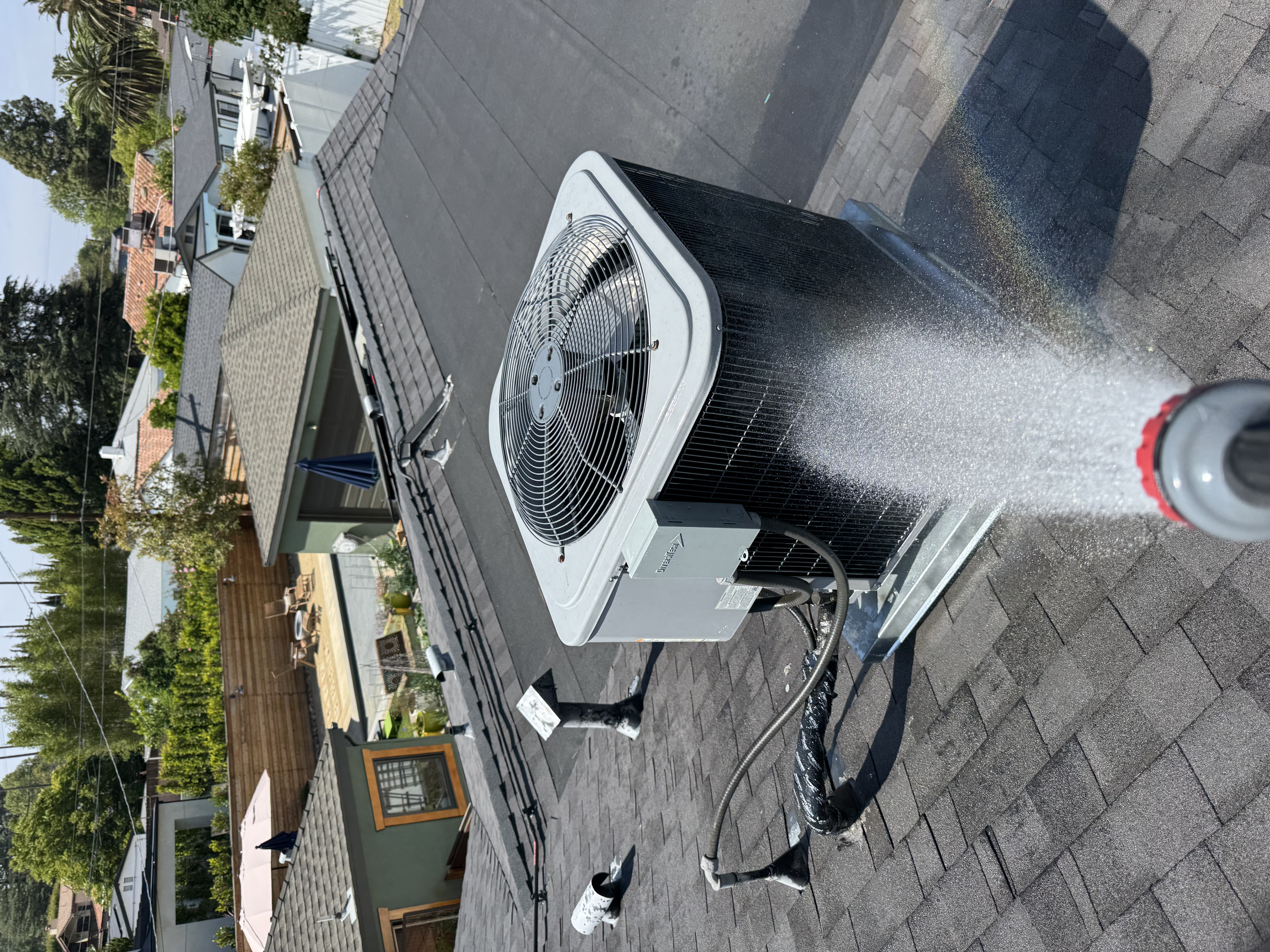 Technician washing and cleaning an outdoor air conditioning condenser unit